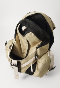 Khaki-Rucksack mit schwarzen Netzelementen und beigen Trägern. Verfügt über eine große Öffnung und mehrere Taschen für Stauraum. Strapazierfähiges Stoffmaterial.