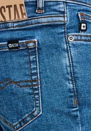 Jeans din denim albastru, cu cusături portocalii, multiple buzunare și un eticheta din piele pe talie, inscripționată "BIG STAR".