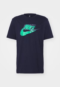 Námořnická modrá krátký rukáv tričko s vrstvenými logy Nike v šedé a zelené barvě uprostřed na přední straně.
