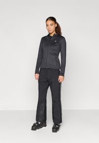 Casaco atlético preto com mangas longas e fecho na frente, emparelhado com calças pretas com riscas laterais, projetadas para atividades ao ar livre.