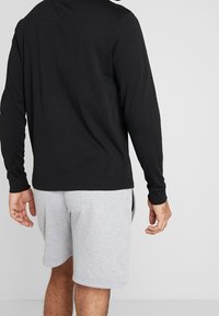 Černé tričko s dlouhým rukávem vyrobené z bavlny, spárované se šedými teplákovými šortkami. Tričko má zaoblený výstřih a upnuté rukávy.