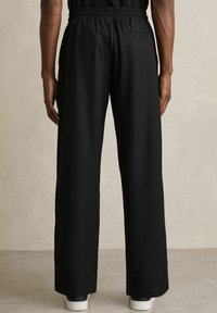 Pantaloni negri, texturati, cu talie largă, dotati cu un brâu elastic și un singur buzunar la spate. Materialul are un model în dungi.