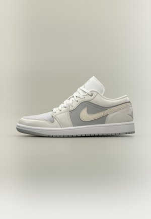Niedrige weiße und hellgraue Nike-Sneaker mit Mesh- und Lederpaneelen sowie einer weißen Gummisohle auf neutralem Hintergrund.