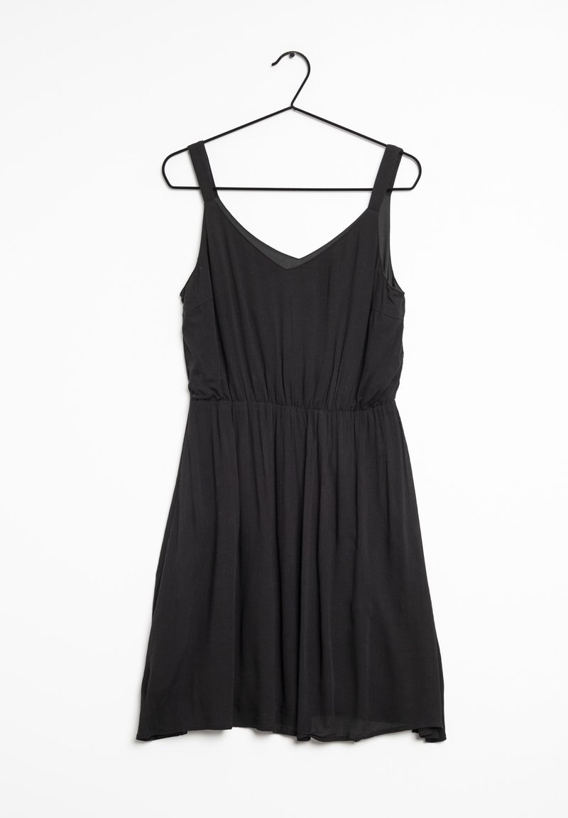 Svart ärmlös klänning med V-ringning, elastisk midja och flödande kjol. Tillverkad av lättviktsmaterial med en mjuk textur. Hänger på en svart krok.