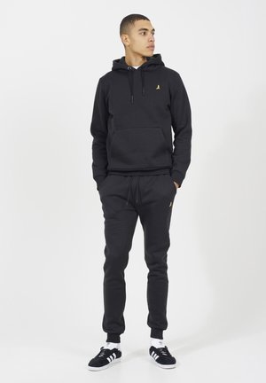 Felpa nera in cotone con tasca a marsupio sul davanti e logo dorato. Abbinata a pantaloni coordinati e sneakers nere con dettagli bianchi.