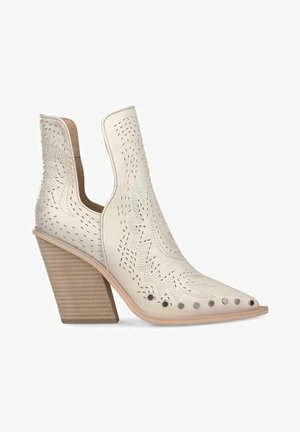 Białe skórzane botki za kostkę z wydłużonym noskiem i wyciętymi bokami. Posiadają perforowane wzory i metalowe ćwieki na cholewce. Masywna, teksturowana obcasa.