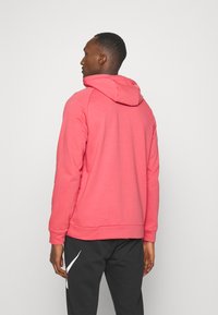 Pink hoodie with a drawstring hood and cuffed sleeves, crafted from soft material. Worn with black pants featuring a white logo.