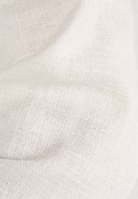 Bílá lněná tkanina s texturovaným vzorem, vykazující jemné záhyby a vrásky. Povrch vypadá lehce a prodyšně.