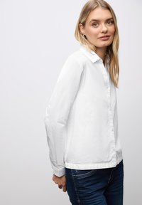 Camisa blanca de manga larga con botones y cuello, hecha de una tela ligera, con un corte recto y textura suave.