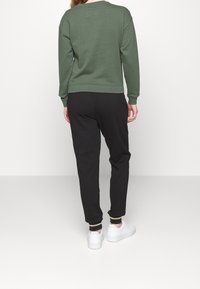 Zelená mikina se žebrovanými manžetami, spárovaná s černými tepláky s elastickým pasem. Na nohou jsou bílé tenisky s tlustou podrážkou.