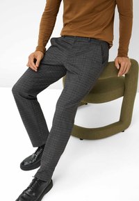 Pantaloni a quadri grigi realizzati in tessuto testurizzato, con una vestibilità slim. Abbinati a un top a maniche lunghe marrone e scarpe stringate nere.