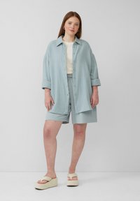 Lichtblauw, textuur shirt met knopen gecombineerd met bijpassende shorts. Heeft opgerolde mouwen en crèmekleurige platform sandalen. Eenvoudige, ontspannen pasvorm.