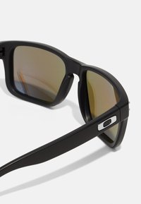 Ochelari de soare negri cu finisaj mat, lentile cu gradient maroniu și un design rectangular elegant. Dispune de accesorii metalice argintii pe brate.