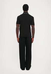 Svart polo skjorte med korte ermer og en kontrastfarge på kragen, kombinert med løse svarte bukser. Teksturedt stoff, enkel design.