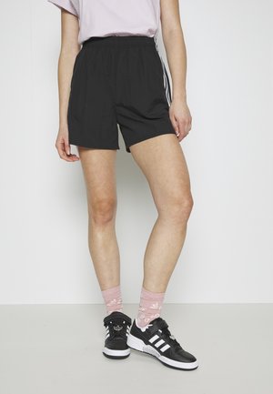 Pantaloni sportivi neri con cintura elastica, abbinati a sneakers neri e calze a fantasia rosa. Tessuto morbido e leggero.