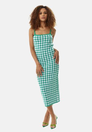 Green and white gingham dress with spaghetti straps, midi length, form-fitting design, textured fabric, paired with green high heels.
