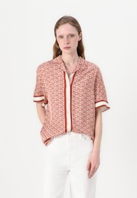 Korte mouwen blouse in koraal met geometrisch patroon, contrasterende witte knopen en afwerking. Lichtgewicht stof met een ontspannen pasvorm.