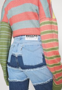 Vaqueros de parches azules con bordes deshilachados, combinados con un suéter de punto multicolor a rayas en tonos rosa, verde y azul.