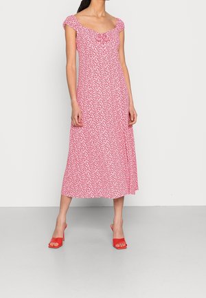 Bloemen midi-jurk in roze met kleine rode bloemen. Schouderstrikjes, getailleerd lijfje, uitlopende rok, gedragen met rode open-toe hakken. Soepele stoftextuur.