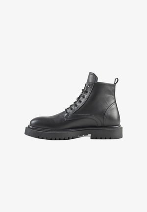 Botas de tobillo de cuero negro con un diseño de cordones, puntera redondeada y una suela de goma negra gruesa con dibujos profundos para mayor tracción.