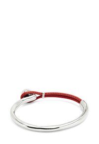 Pulsera rígida de plata con una correa de cuero rojo que se loopa a través de un anillo de metal, asegurada por un pequeño cierre de plata.