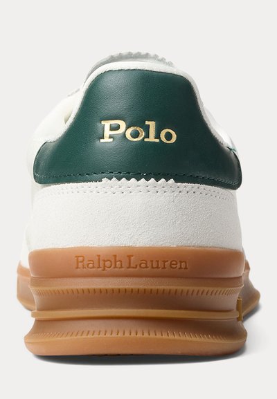 Biela a zelená päta tenisky s podrážkou z gumy, nápis „Polo“ zlatou farbou na zelenej koži a „Ralph Lauren“ vyrazené na gumenej podrážke.