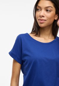 Královsky modré tričko s krátkým rukávem a kulatým výstřihem, vyrobené z měkké látky. Obsahuje ohrnuté manžety rukávů a má pohodlný střih.