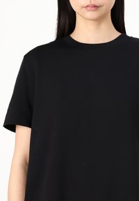 T-shirt noir en coton avec des manches courtes et un col rond. Texture lisse et coupe décontractée, sans motifs ni accents visibles.