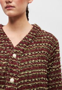 Červený a zelený textúrovaný cardigan s výstrihom do V, ozdobený tromi dekoratívnymi perlovými gombíkmi a jemnými flitrami po celej úprave látky.