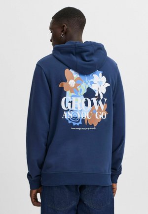 Navy blue hoodie with a floral graphic print on the back, featuring text "GROW AS YOU GO" and various colored flowers in soft textures.