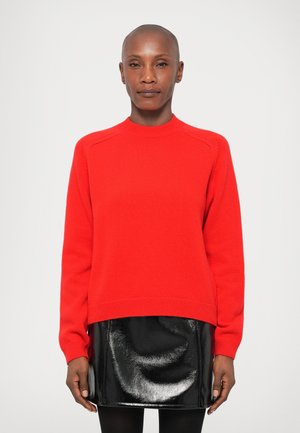 Rød strikket sweater med høj hals og ribbede manchetter, parret med en skinnende sort læder miniskørt. Enkel, moderne design.