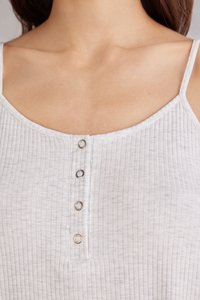 Bílý žebrovaný top bez rukávů s kulatým výstřihem a čtyřmi kovovými knoflíkovými detaily na přední straně. Nastavitelné ramínka.