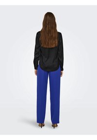 Blouse en satin noir à manches longues, associée à un pantalon taille haute bleu vif. Les deux pièces ont une texture lisse et une coupe ajustée.