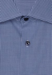 Chemise à carreaux bleue avec fermeture à bouton, dotée d'un col et d'une texture lisse. Le motif est composé de petits carrés uniformément espacés.