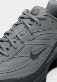 Κοντινή λήψη γκρι αθλητικού παπουτσιού με υφή υφάσματος, διασταυρούμενα κορδόνια και λογότυπο σήματος "swoosh" στο πλάι κοντά στη γλώσσα και τη σόλα.