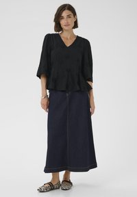 Schwarze Peplum-Bluse mit gemustertem Muster, kombiniert mit einem langen Jeansrock und schwarz-weißen flachen Schuhen mit Streifen.