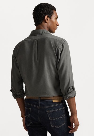 Pelēka kokvilnas krekliņa ar sarullētām piedurknēm, muguras yoke detaļa, apvienots ar tumšiem denim džinsiem ar redzamām šuvēm un kabatu detaļām.