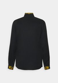 Camisa negra de manga larga con un cuello y puños decorativos en patrón amarillo y negro. Textura suave, corte estructurado y diseño minimalista.