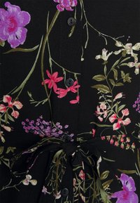 Blommig klänning med svart bakgrund, livfulla rosa och lila blommor, knappstängning och knut vid midjan. Mjuk tygtextur.
