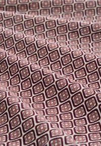 Tissu en coton présentant un motif géométrique répété de carrés bordeaux et bleu clair sur fond crème, avec une texture lisse.
