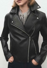 Czarna skórzana kurtka motocyklowa ze srebrnymi zamkami błyskawicznymi, zatrzaskami i kołnierzem z wcięciem. Charakteryzuje się dopasowanym krojem i gładką fakturą.