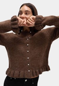 Brązowy, fakturowany sweter dzianinowy z okrągłym dekoltem, zapięcie na guziki z perłowymi akcentami oraz ściągacze na mankietach i u dołu.