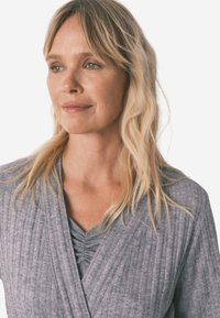 Top gris à rayures avec un décolleté en V profond et une texture douce. Caractéristiques : détails froncés au niveau de la poitrine et manches longues.