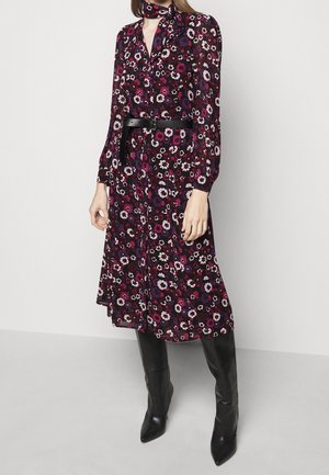 Woman wearing a long-sleeve, floral midi dress with a black belt and matching scarf, paired with black knee-high boots.