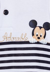 Mickey Mouse schaut über schwarz-weiße horizontale Streifen, auf denen das Wort "Adorable" in goldener Schrift auf weißem Stoff gestickt ist.