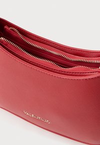 Crvena Valentino torba s glatkom teksturom, dva odvojena džepa s patent-zatvaračem i zlatnim hardverom s brandingom sprijeda.