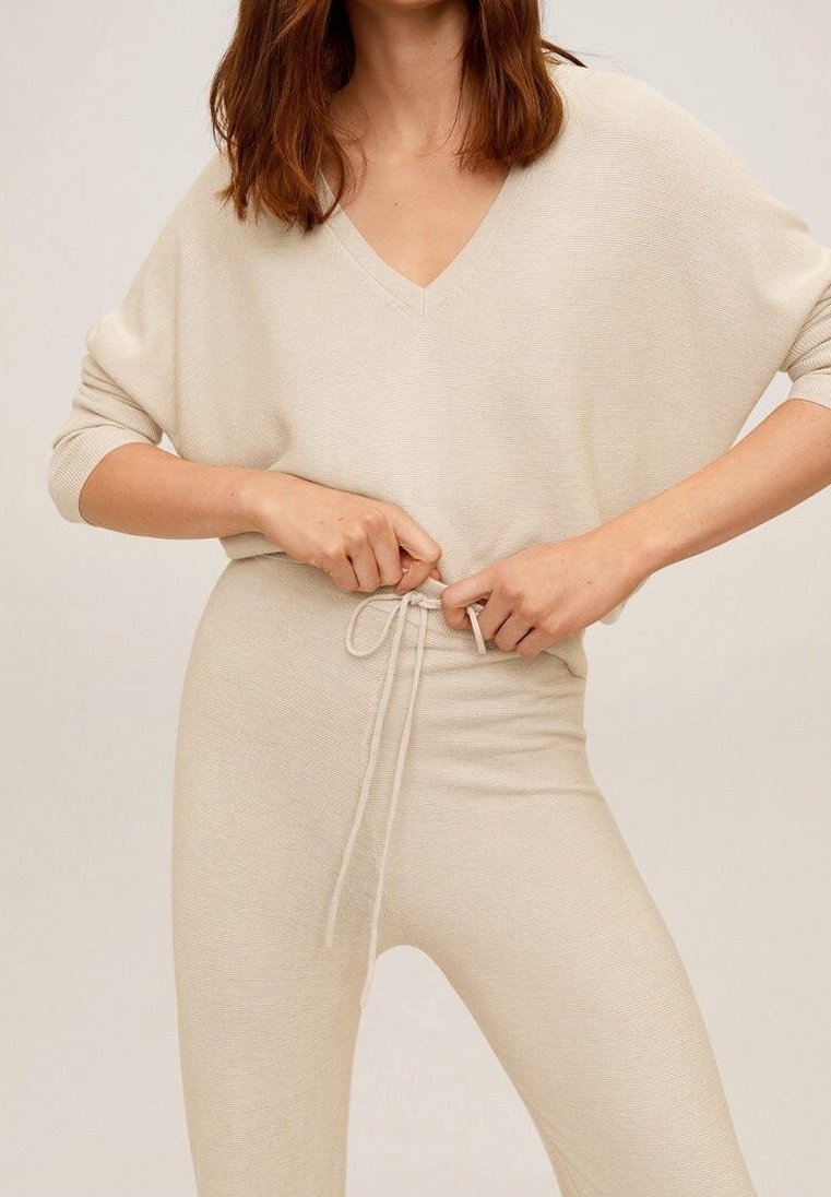 Pull beige en tricot avec col en V et manches larges, associé à un pantalon à cordon de serrage assorti. Texture lisse et coupe décontractée.