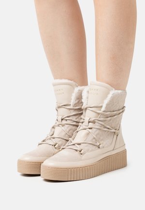 Bottes d'hiver beiges à lacets avec semelles en caoutchouc épaisses, côtés matelassés et doublure pelucheuse portées sur des jambes nues.