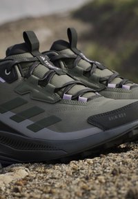 Green hiking shoes with a textured upper, reflective accents, and a sturdy rubber sole. Visible lacing system and "RAIN.RDY" branding.