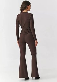 Brązowy bodysuit z długim rękawem z marszczonym wykończeniem na plecach, zestawiony z dopasowanymi spodniami w kształcie dzwonów, wykonanymi z gładkiego, elastycznego materiału.
